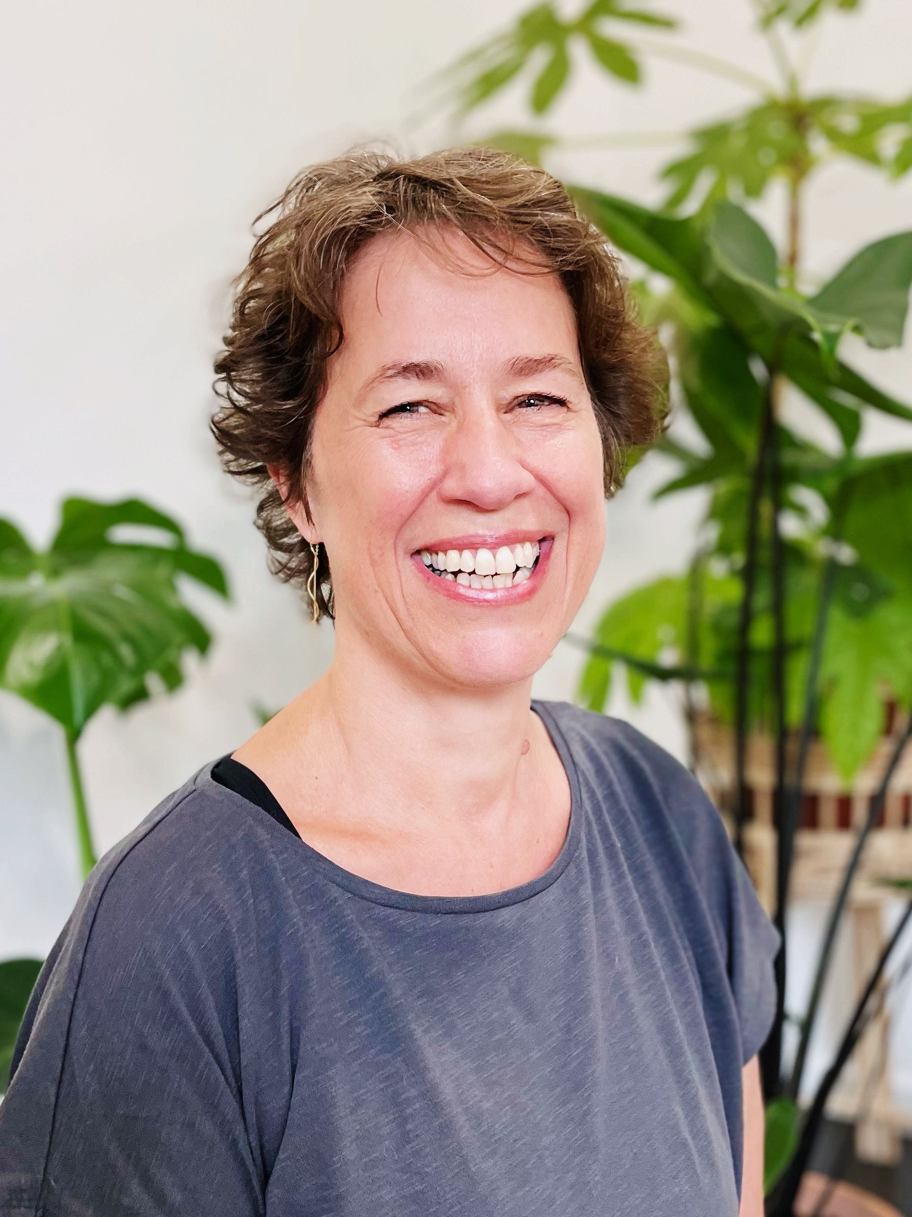 Underviser Hanneloa i en grå bluse smiler foran en plante.