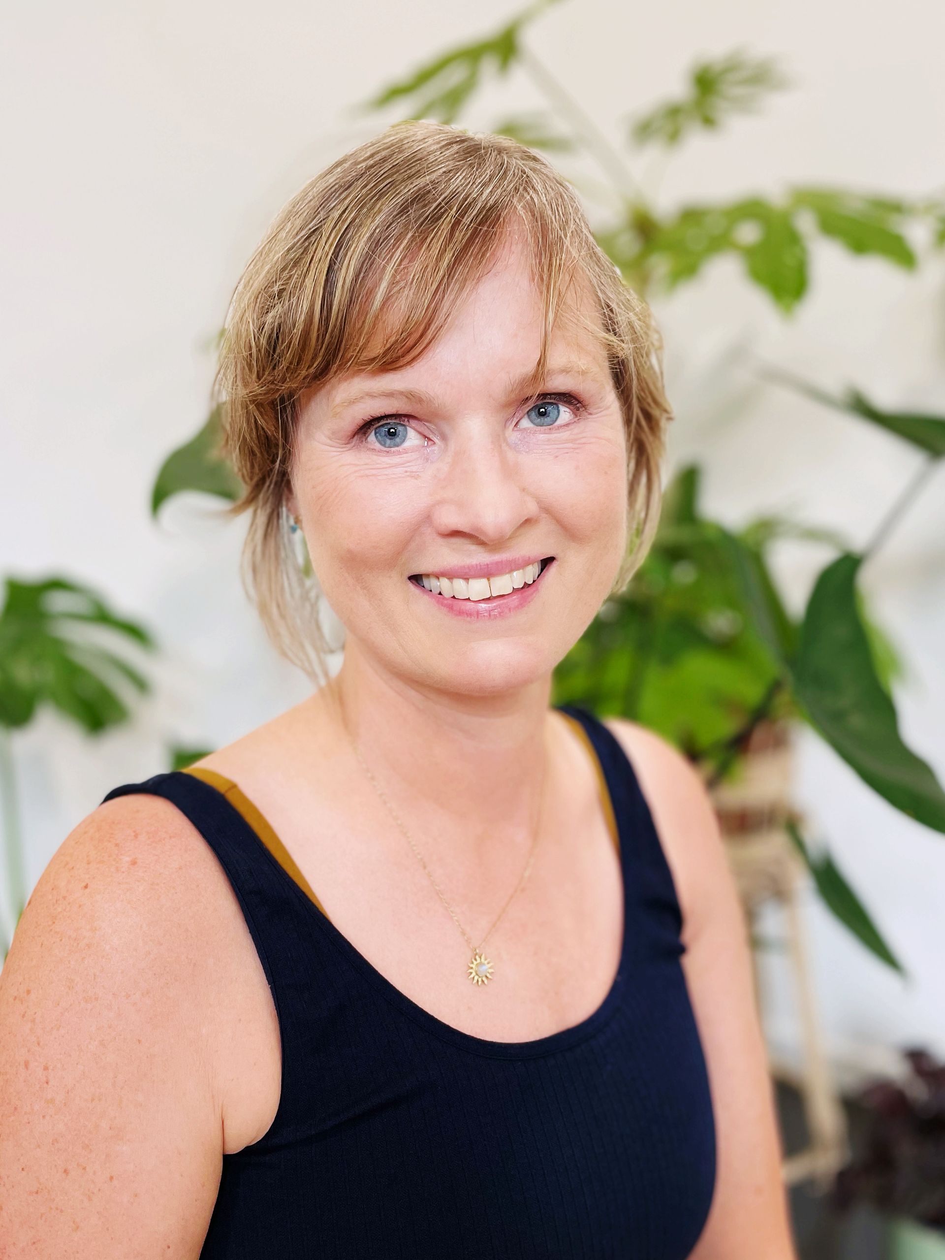 Underviser June i en sort tanktop smiler foran en plante.