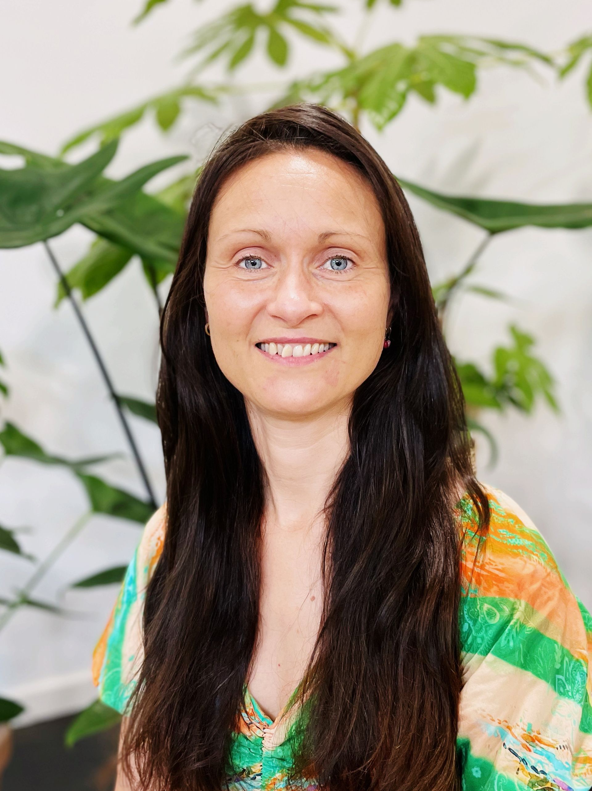 Underviser Helle med langt sort hår og blå øjne smiler foran en plante.