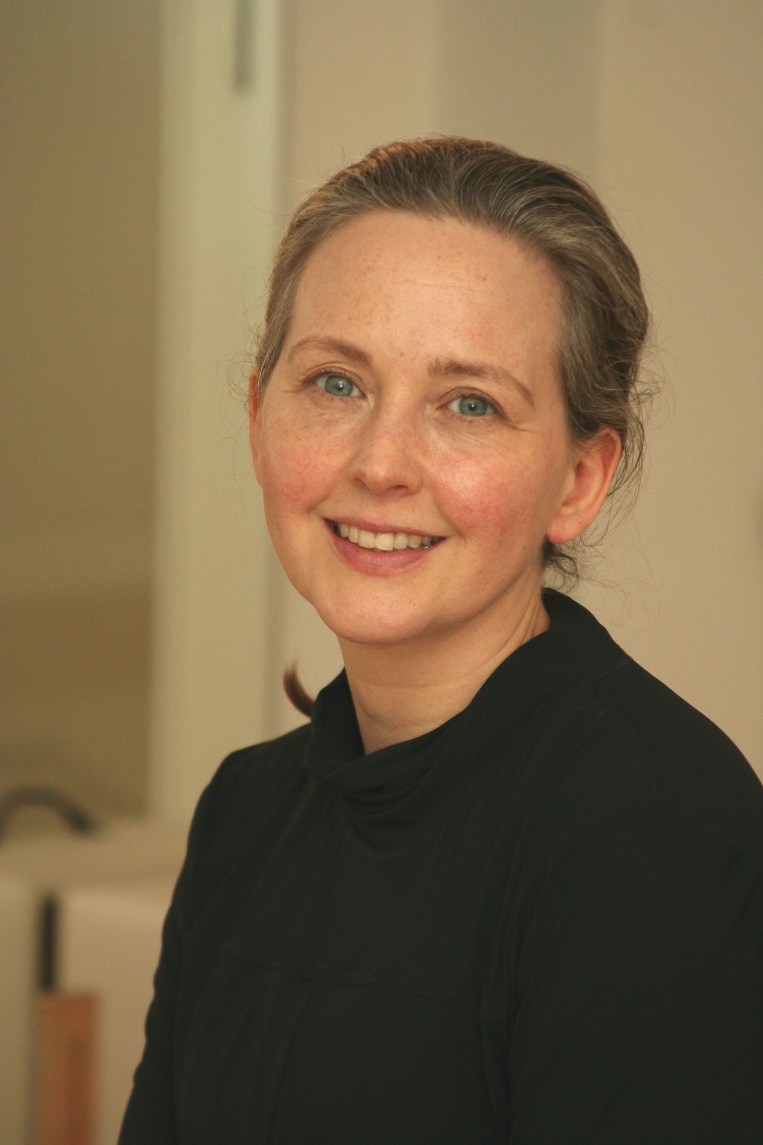 Underviser Louise med stort krøllet brunt hår smiler stort foran en potteplante.