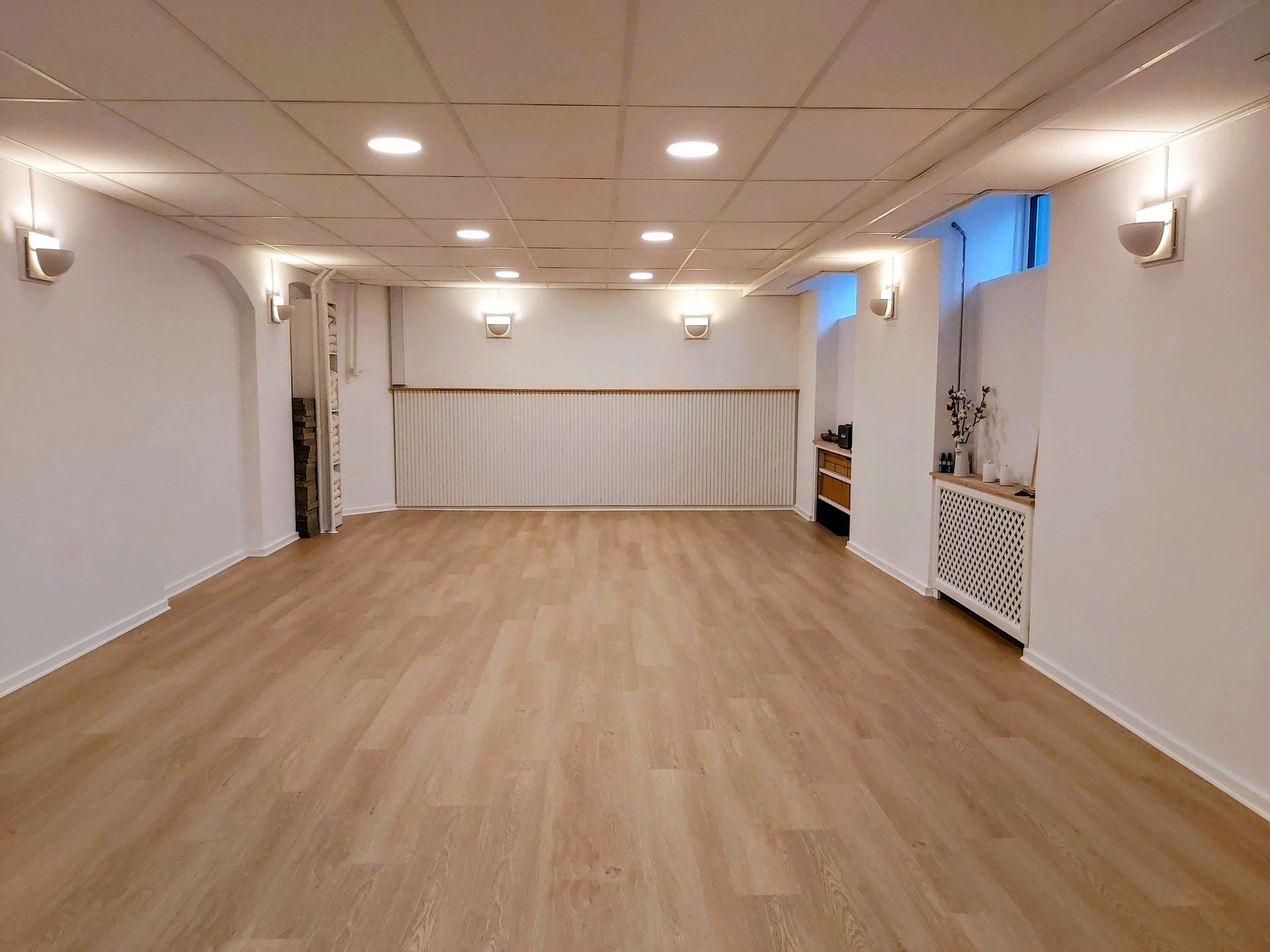 Et stort tomt rum med trægulve og hvide vægge.