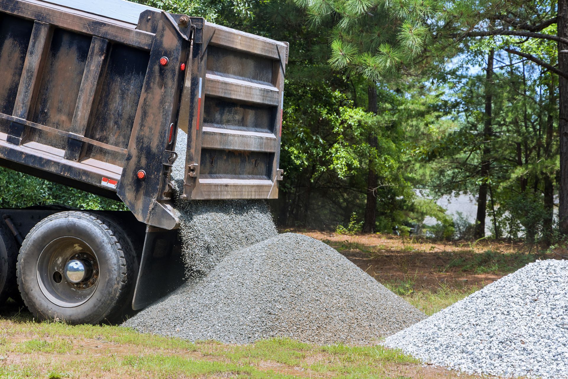 A dump truck unloading a gravel pile on grass during landscaping rock delivery for yard use