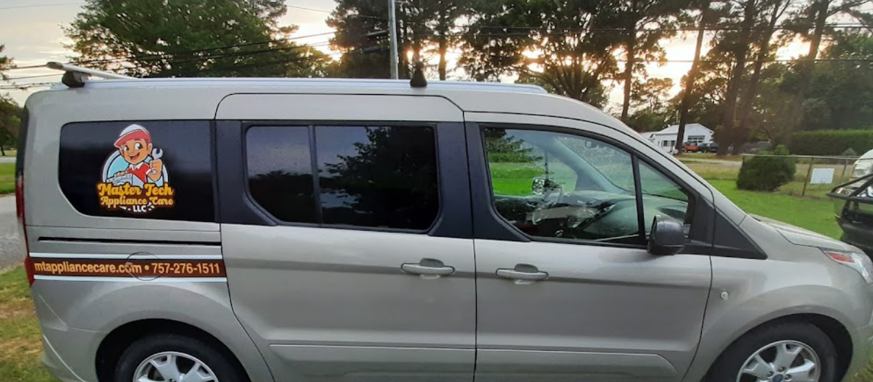 A silver van is parked in a grassy area with trees in the background.