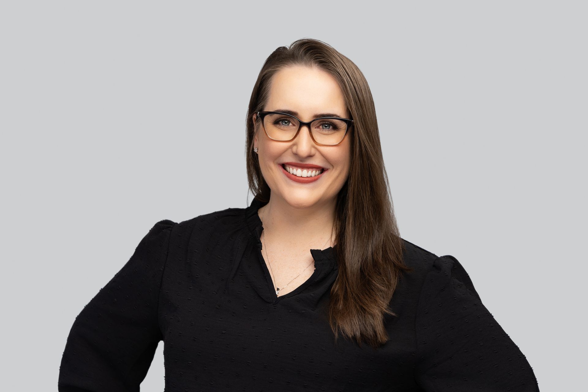 A woman wearing glasses and a black sweater is smiling for the camera.