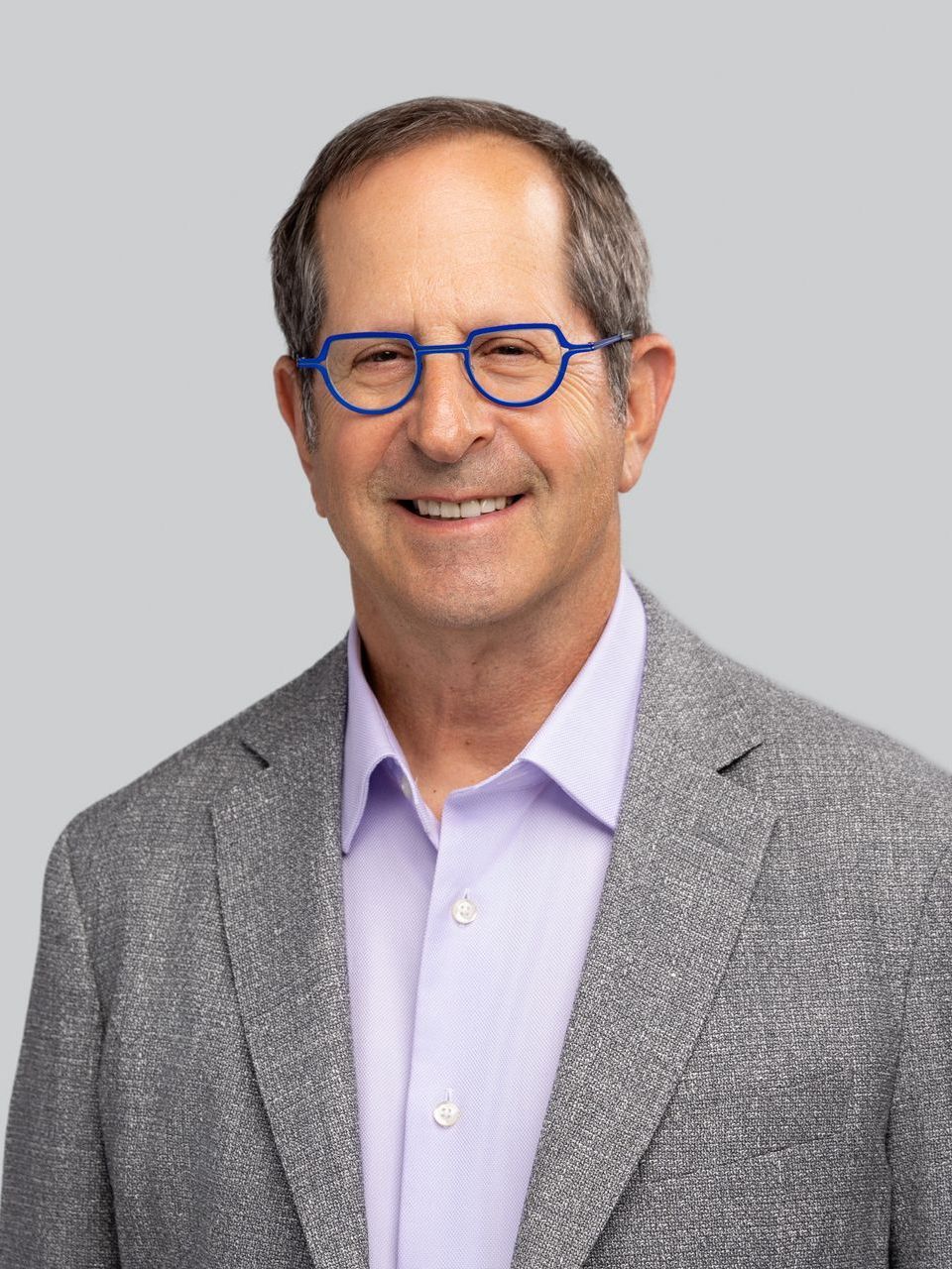 A man wearing glasses and a gray jacket is smiling for the camera.