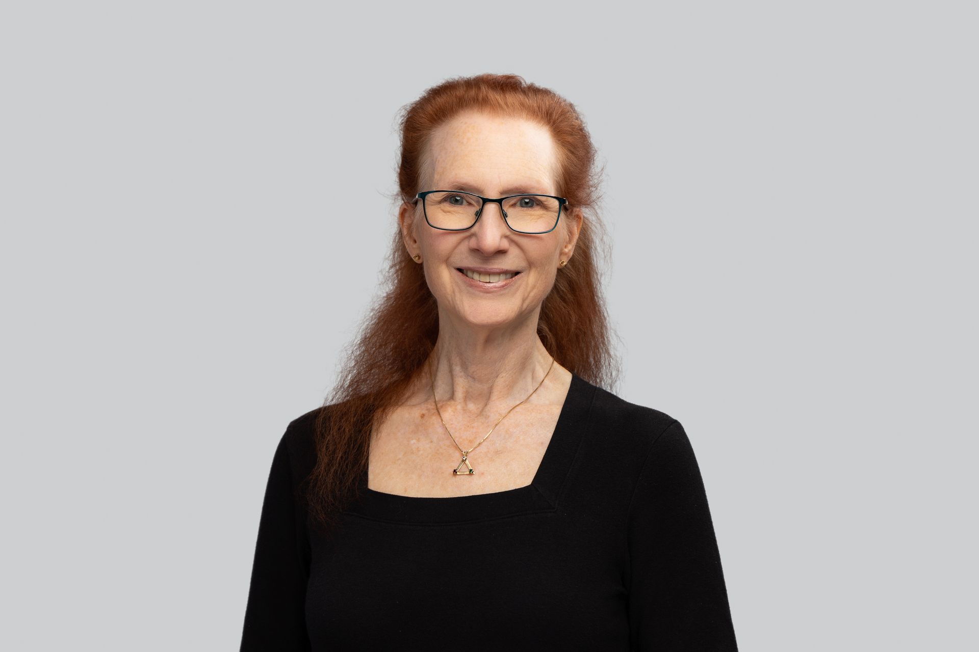 A woman with red hair and glasses is wearing a black shirt and smiling.