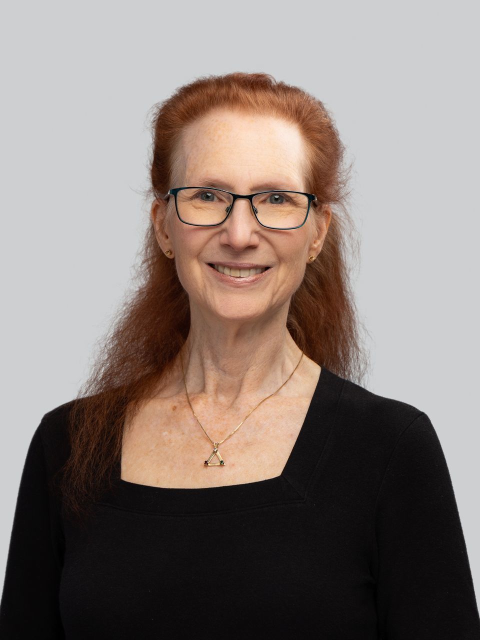 A woman with red hair is wearing glasses and a black shirt.