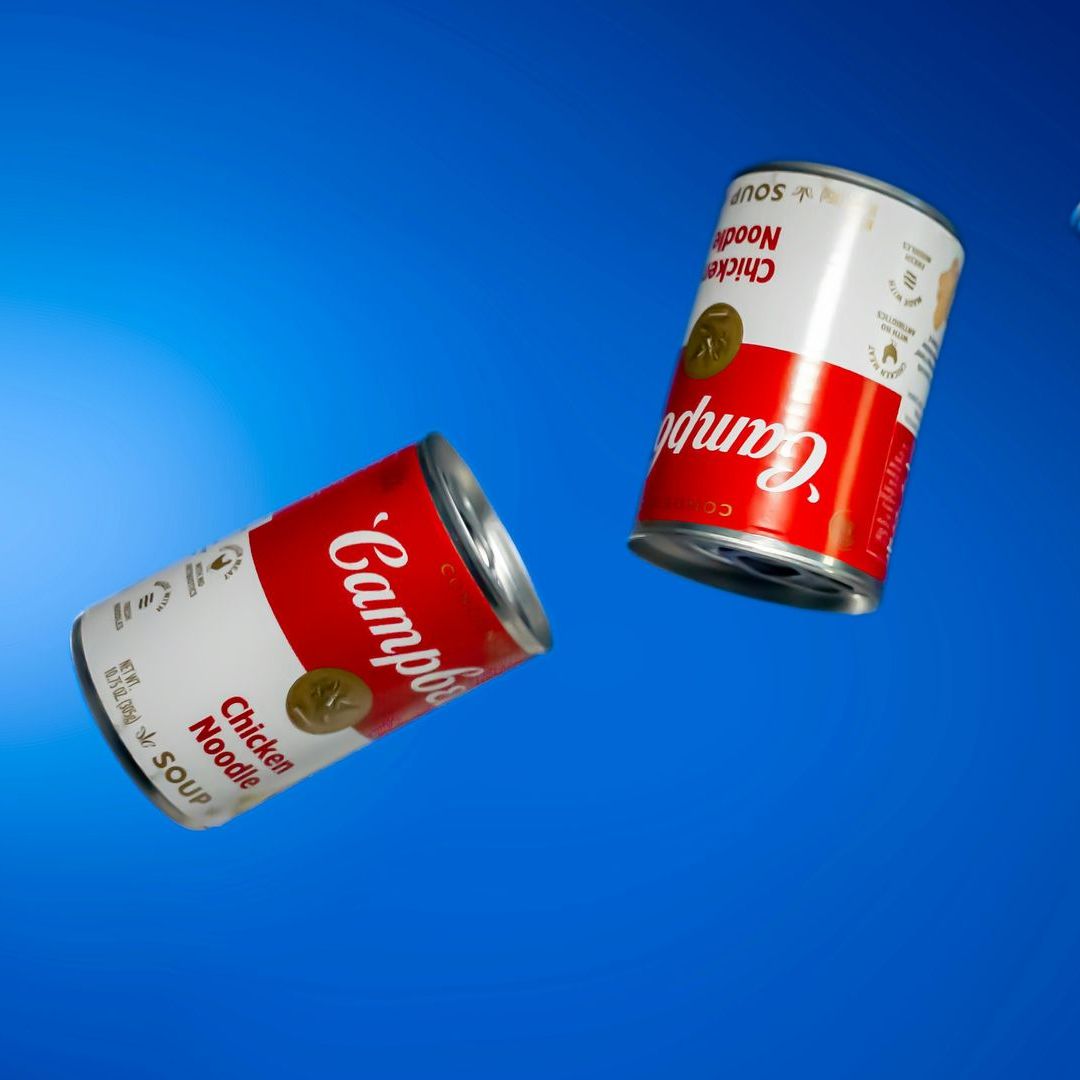 Two cans of campbell 's chicken noodle soup are floating in the air