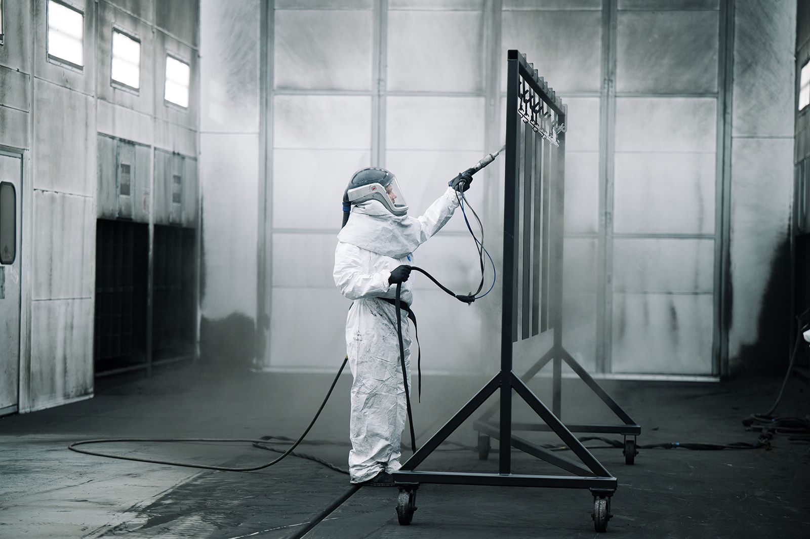 Technician in complete PPE applying electrostatic powder coating for a durable, uniform industrial finish.