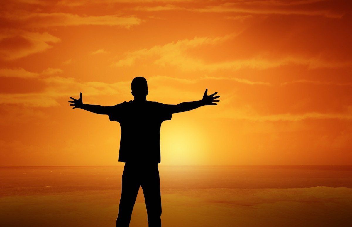 A silhouette of a man standing with his arms outstretched in front of a sunset.