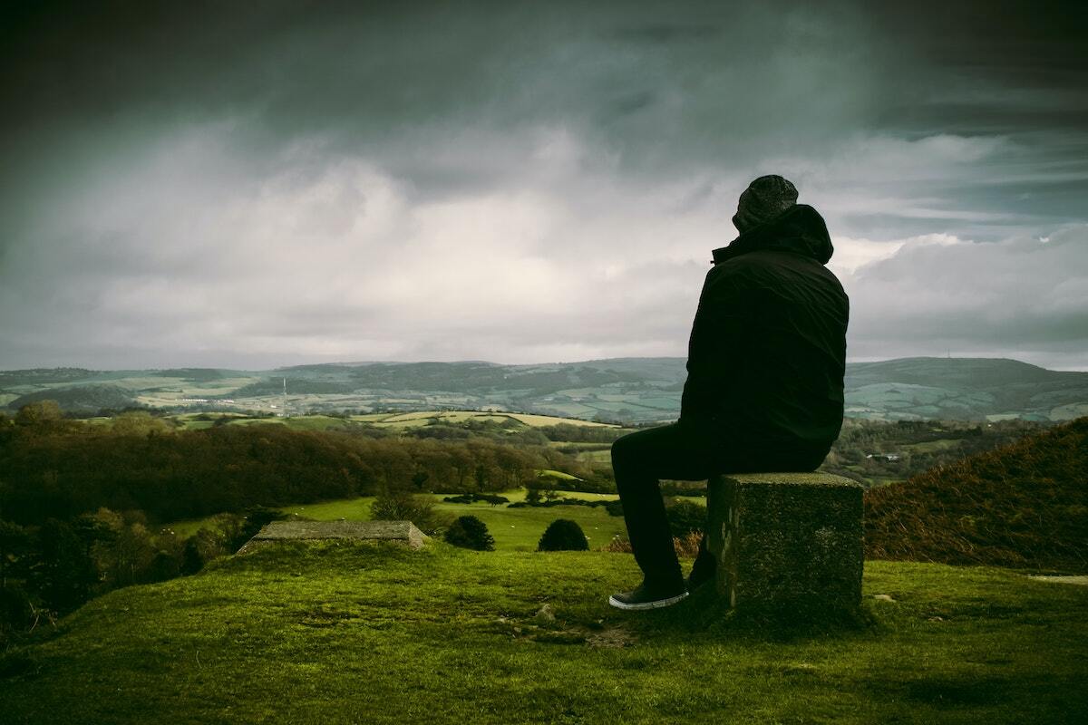 A man is sitting on a stump in the middle of a field.