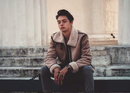 A young man in a jacket is sitting on a set of stairs.