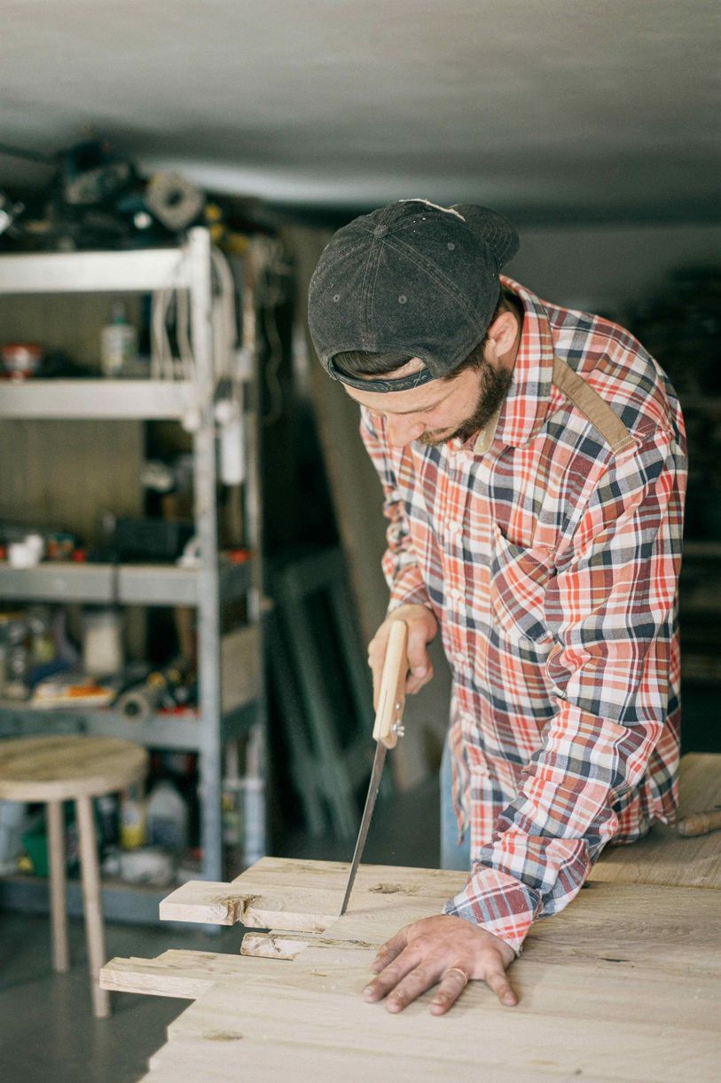 A man in a plaid shirt is working on a piece of wood.