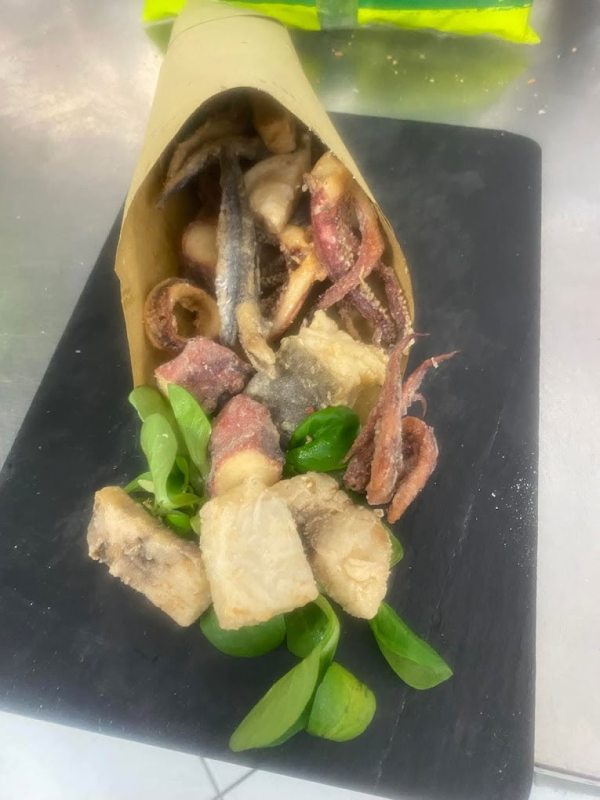 Un cono pieno di cibo fritto è su un tagliere.
