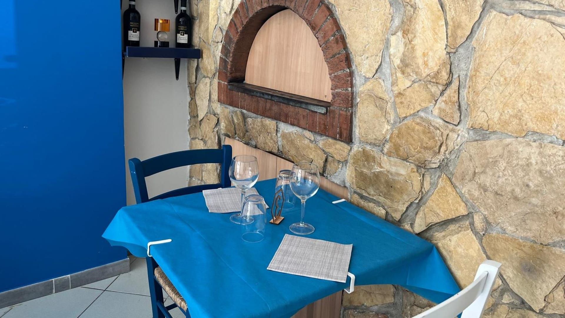 Un tavolo con una tovaglia blu e dei bicchieri sopra, di fronte a un muro di pietra.