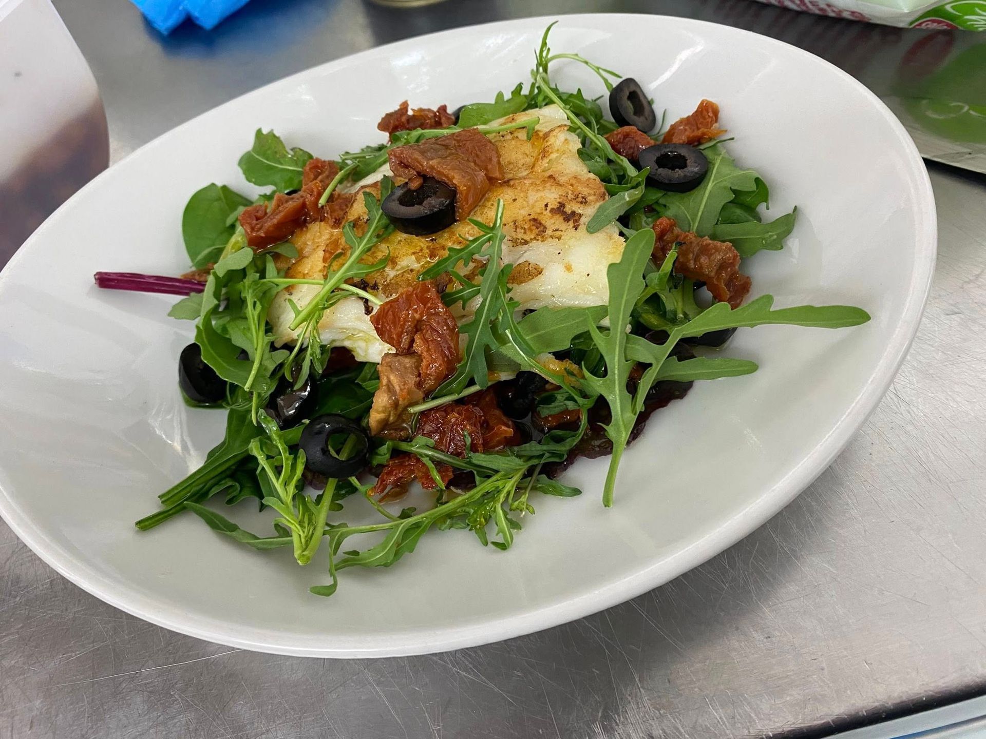 Un piatto bianco con sopra un'insalata di lattuga, olive e formaggio.
