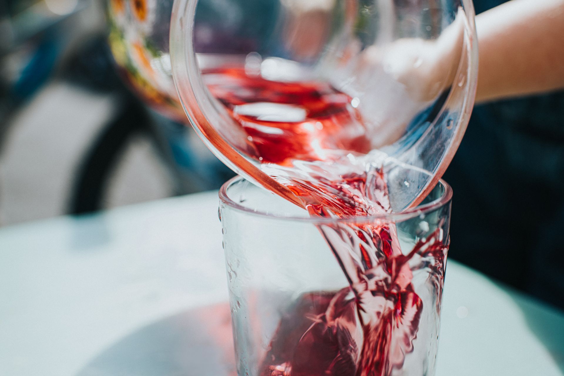 Una persona sta versando del liquido rosso in un bicchiere su un tavolo.