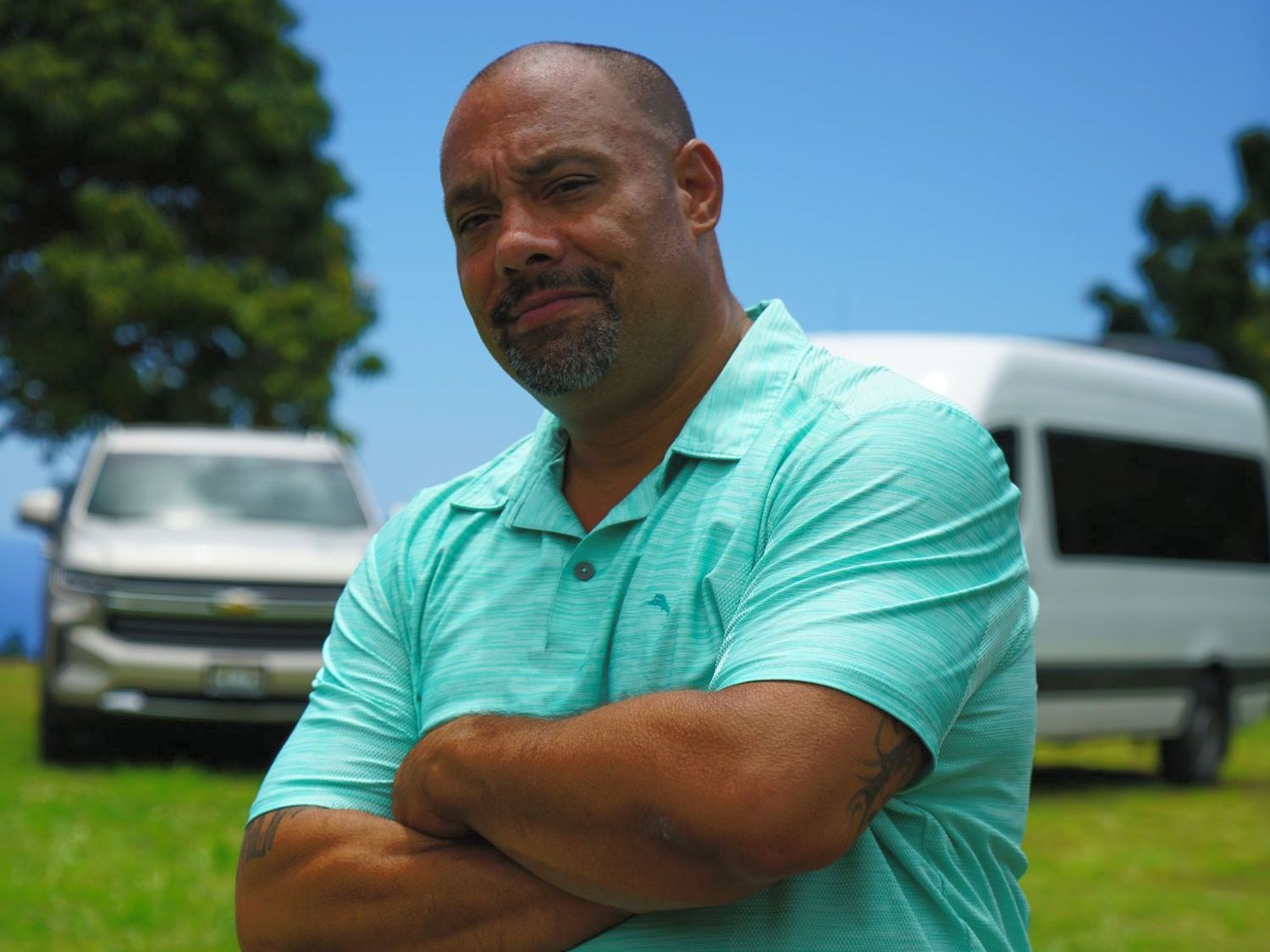 A man in a green shirt is standing with his arms crossed in front of a trailer.