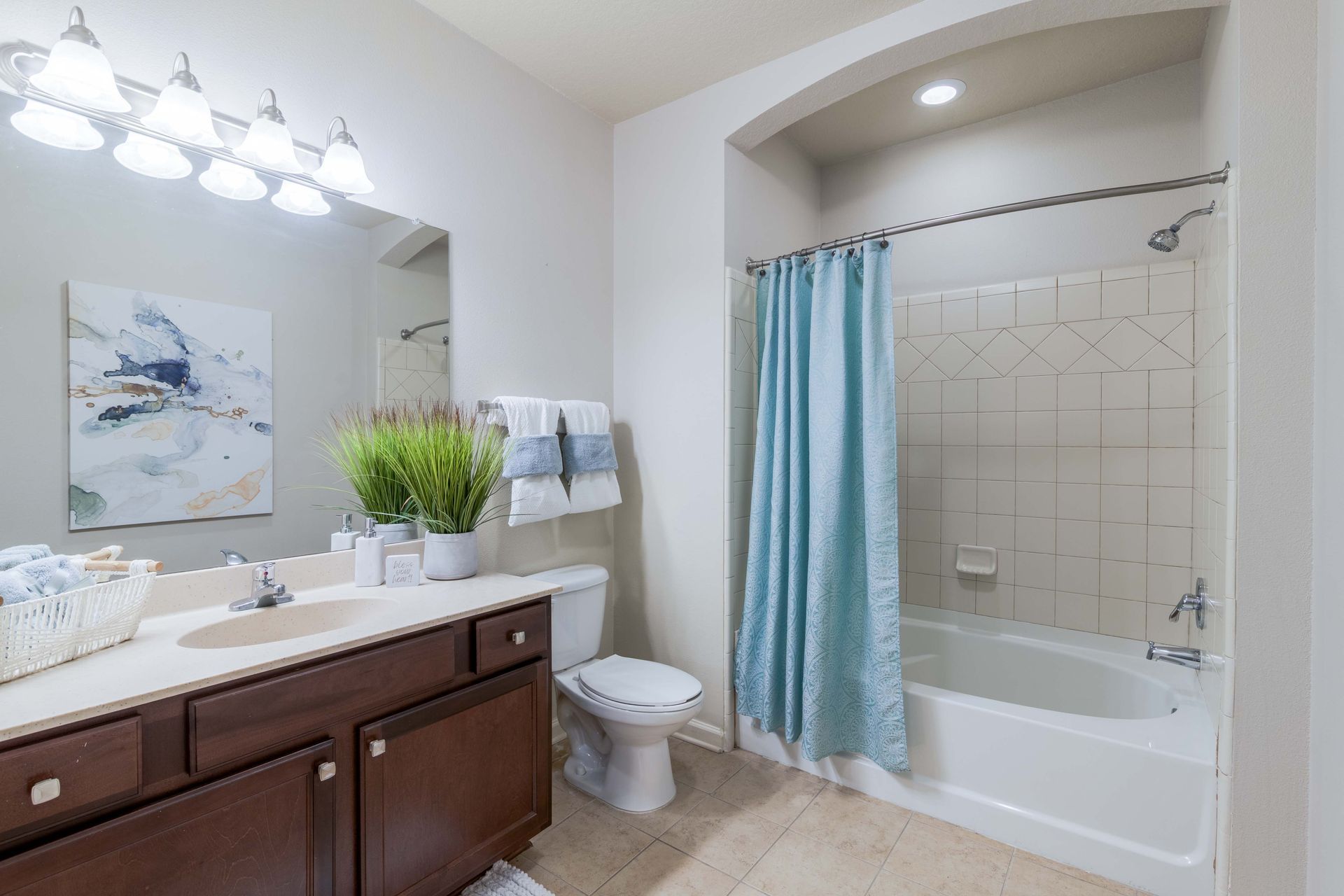 Bathroom with a brown vanity, white toilet, and a bathtub with a blue shower curtain at Grand Oaks at Ogeechee River, offers apartments in Savannah, GA.