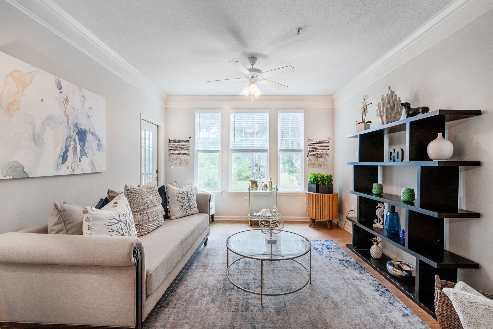 Living room with sofa, coffee table, shelves, window, artwork, and a rug at Grand Oaks at Ogeechee River, offers apartments in Savannah, GA.