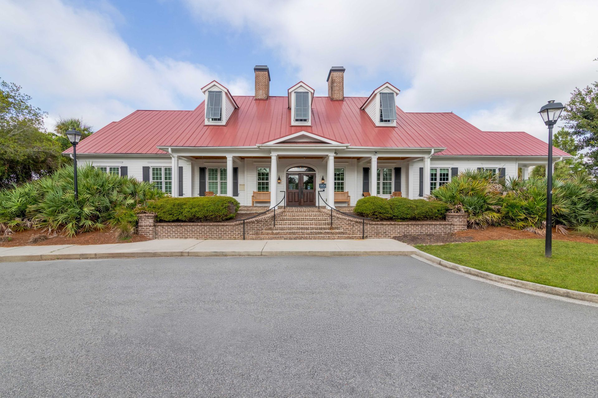White building with red roof, porch, and dormers; driveway and landscaping in front at Grand Oaks at Ogeechee River, offers pet-friendly apartments for rent in Savannah, GA.