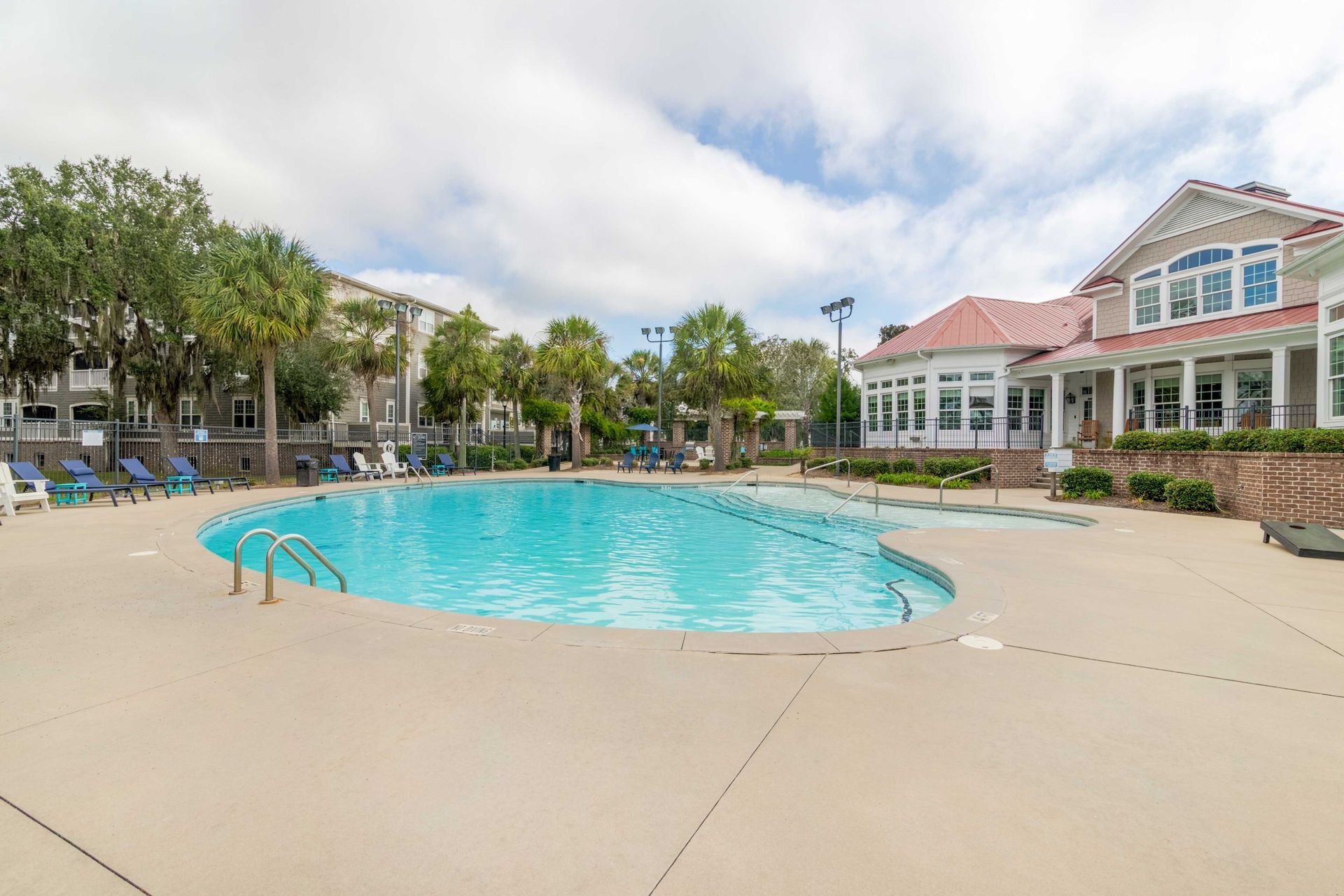 Swimming pool with lounge chairs, trees, and building under a cloudy sky at Grand Oaks at Ogeechee River, offers pet-friendly apartments for rent in Savannah, GA.