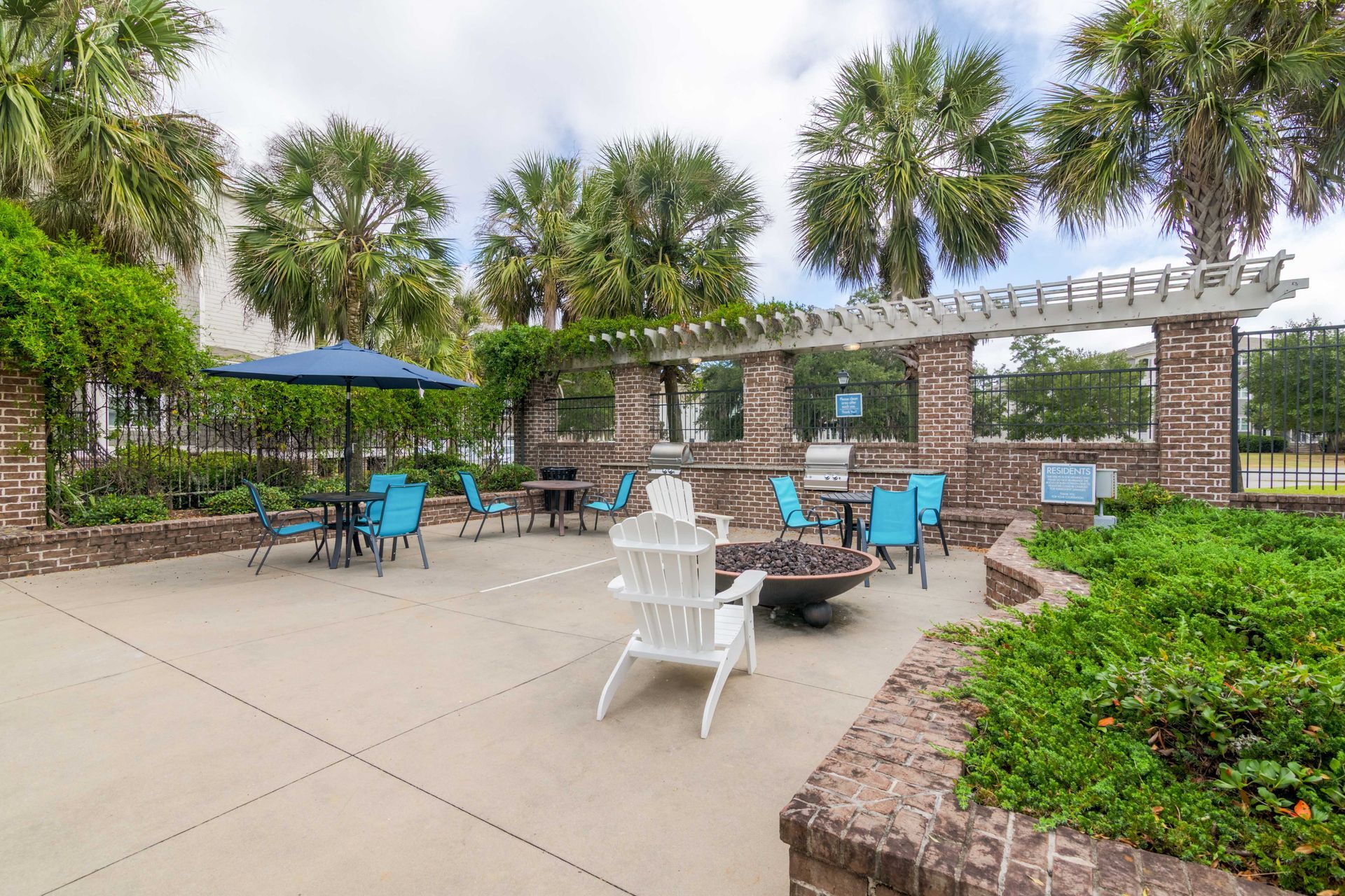 Outdoor patio with blue chairs, fire pit, grill, and pergola under palm trees at Grand Oaks at Ogeechee River, offers pet-friendly apartments for rent in Savannah, GA.