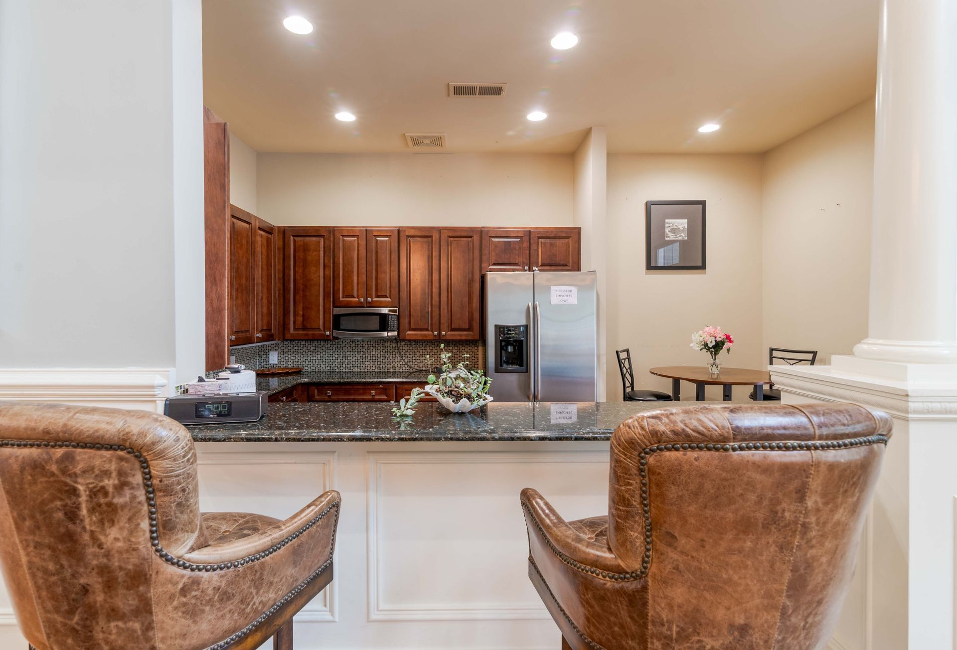 Two leather chairs face a kitchen with wood cabinets, stainless steel appliances, and a table with flowers at Grand Oaks at Ogeechee River, offers apartments for rent in Savannah, GA.