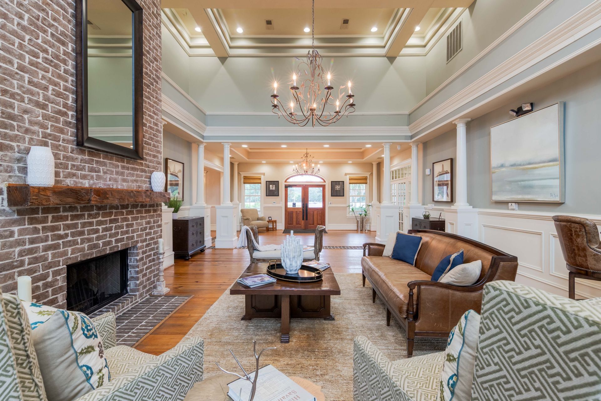 Clubhouse with fireplace, brown leather sofa, rug, chandelier, and entryway with double doors at Grand Oaks at Ogeechee River, offers apartments for rent in Savannah, GA.