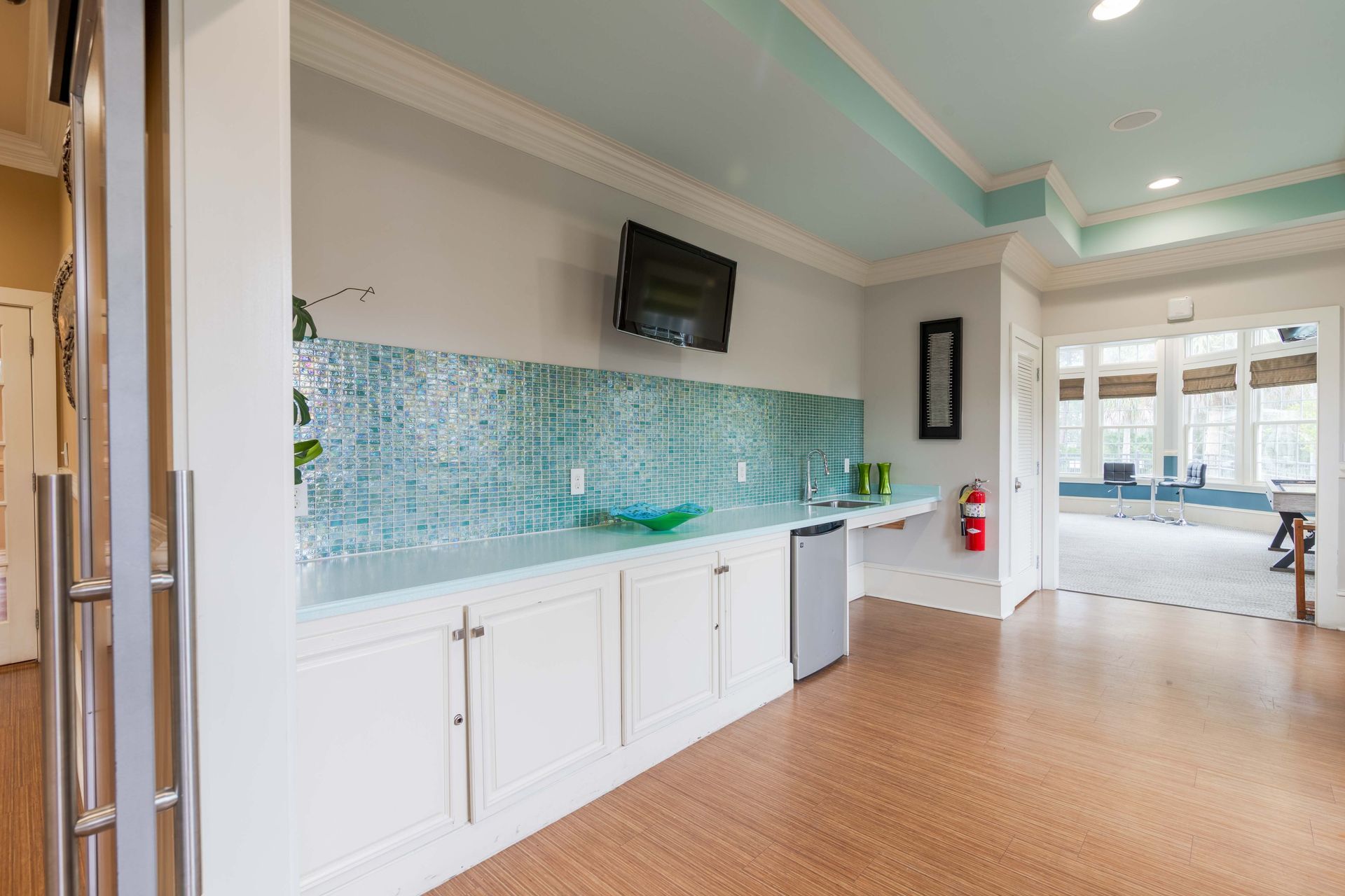 Kitchenette with a blue tile backsplash, small fridge, and a TV mounted on the wall at Grand Oaks at Ogeechee River, offers apartments for rent in Savannah, GA.