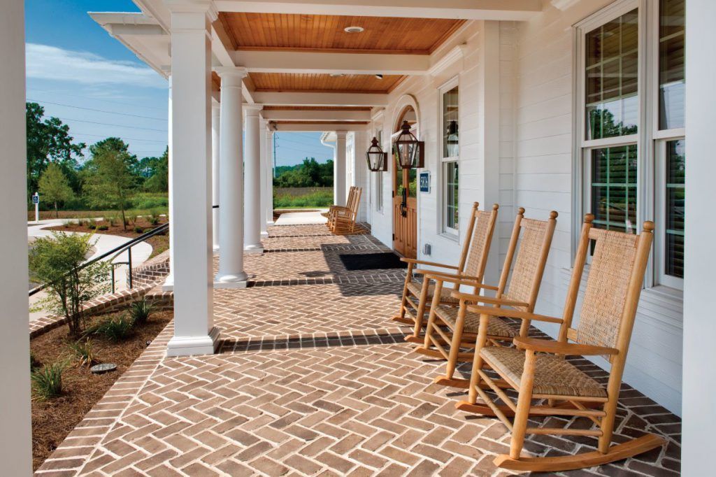 A porch with rocking chairs in front of a white building at Grand Oaks at Ogeechee River, offers apartments in Savannah, GA.
