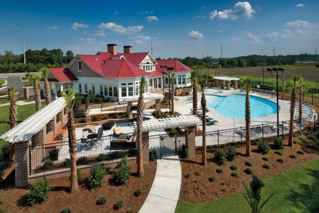 Clubhouse with red roof, pool, and palm trees in outdoor setting at Grand Oaks at Ogeechee River, offers pet-friendly apartments for rent in Savannah, GA.