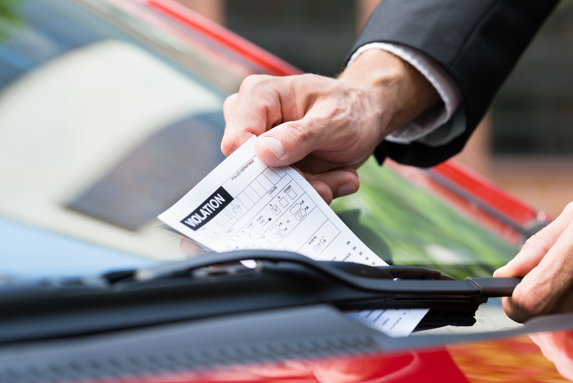 A person is putting a parking ticket on the windshield of a car.