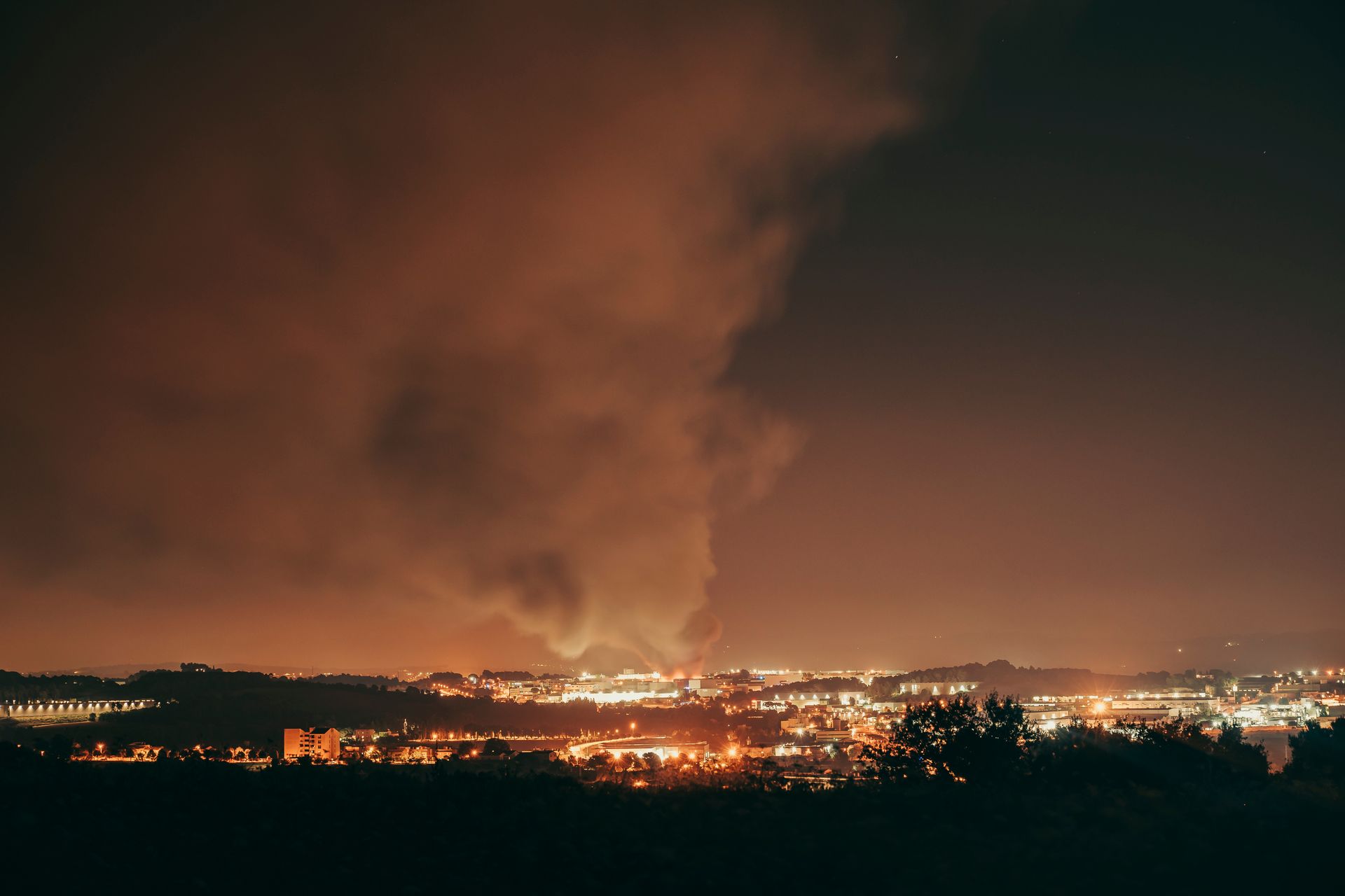 A large cloud of smoke is coming out over a city at night.
