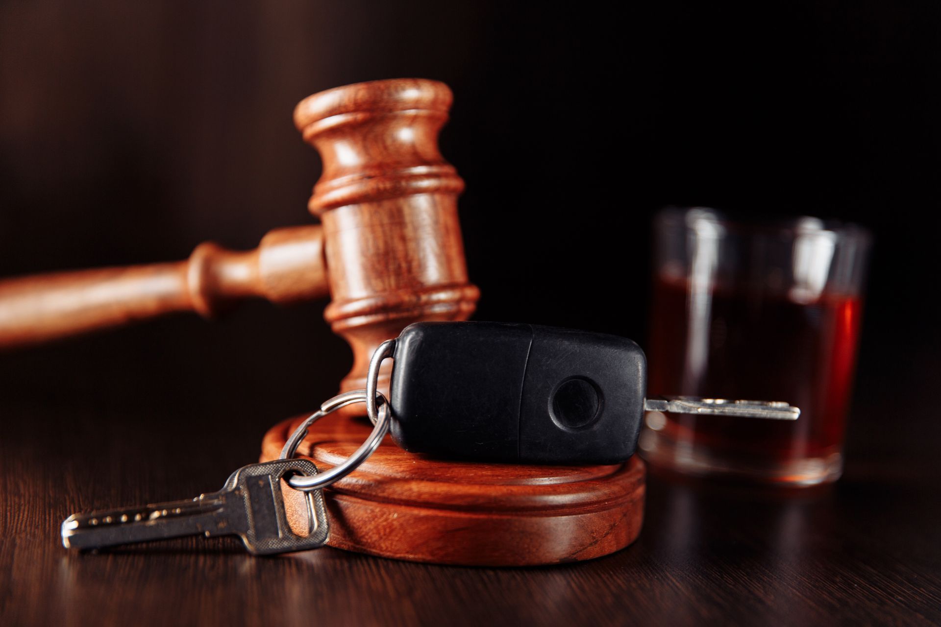 A car key sitting on top of a wooden gavel next to a glass of alcohol.