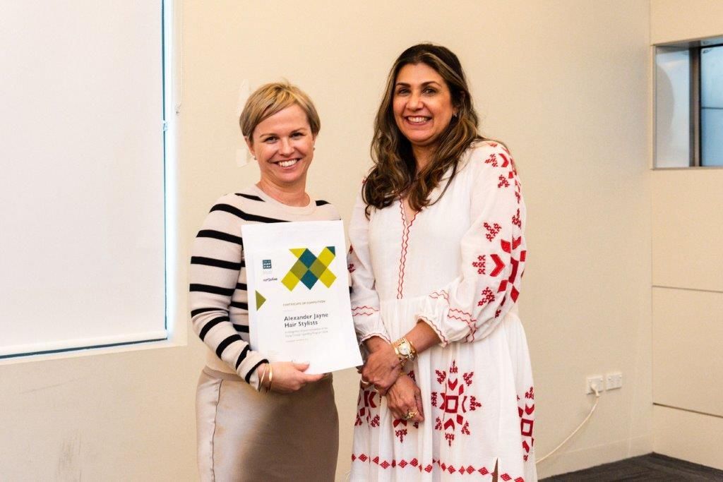 Two women are standing next to each other in a room holding a certificate.