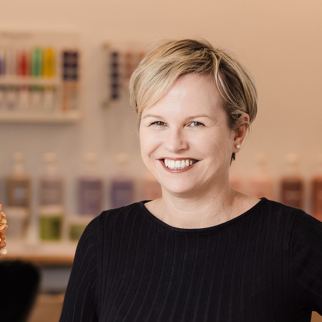 A woman is standing behind a counter in a hair salon holding a vase of flowers.