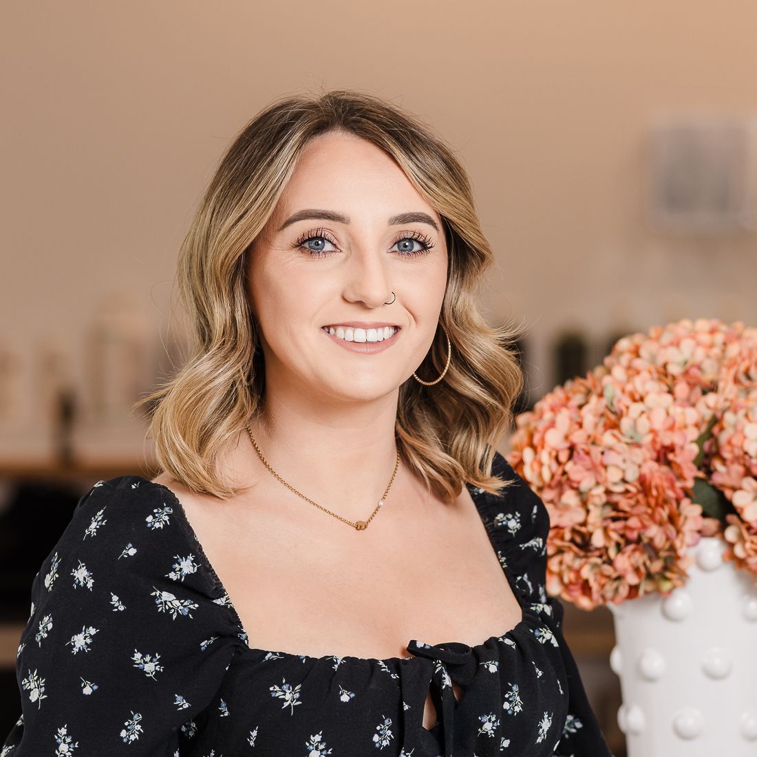 A woman in a black dress is standing in a salon next to a vase of flowers.