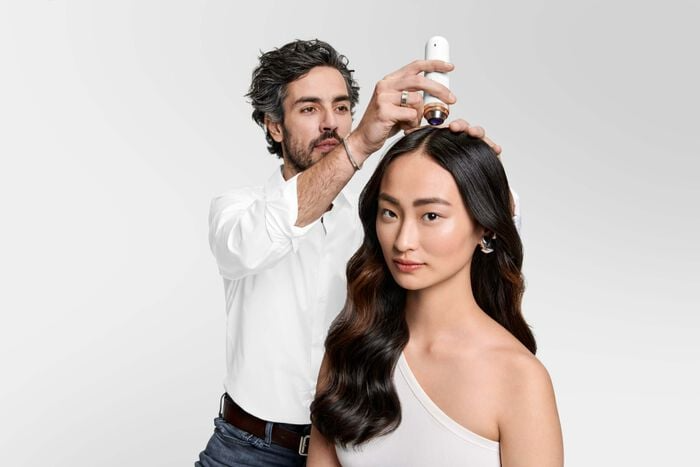 A man is spraying a woman 's hair with a spray bottle.