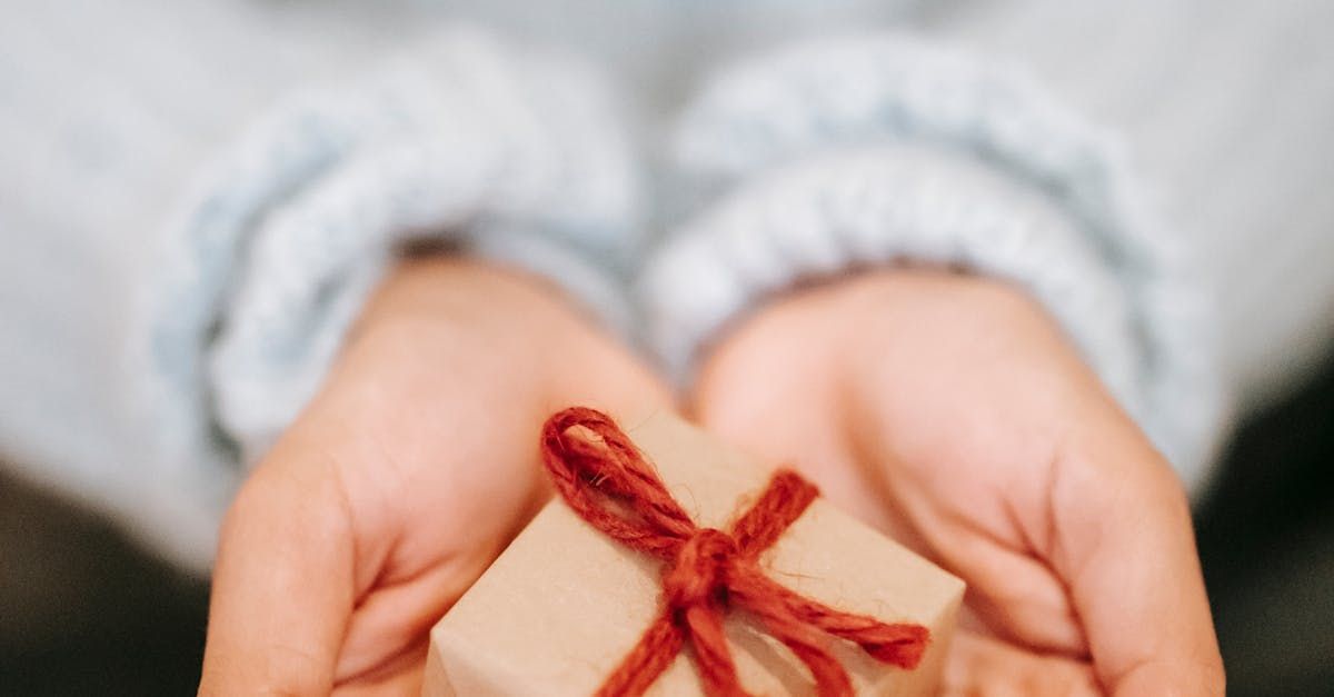A person is holding a small gift box with a red ribbon in their hands.