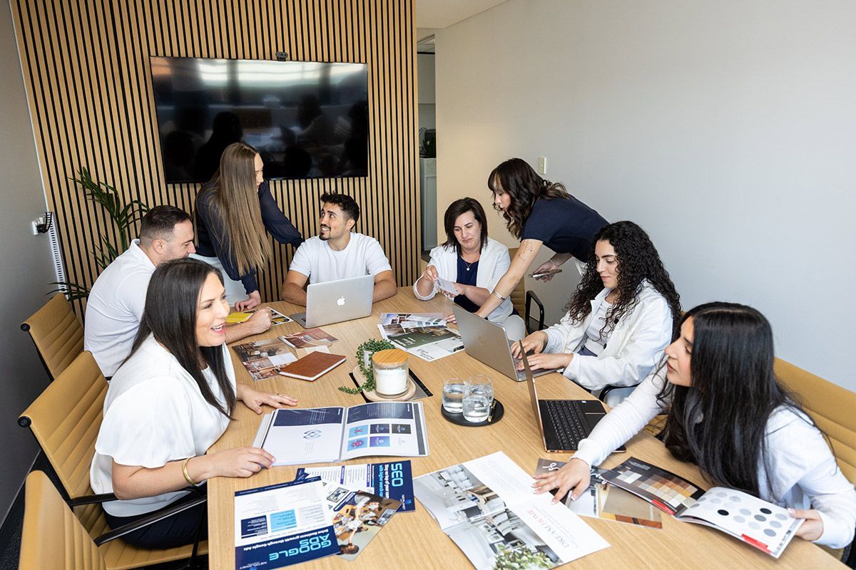 Group of people in a meeting. They are gathered around a table with laptops, papers, and coffee discussing SEO.