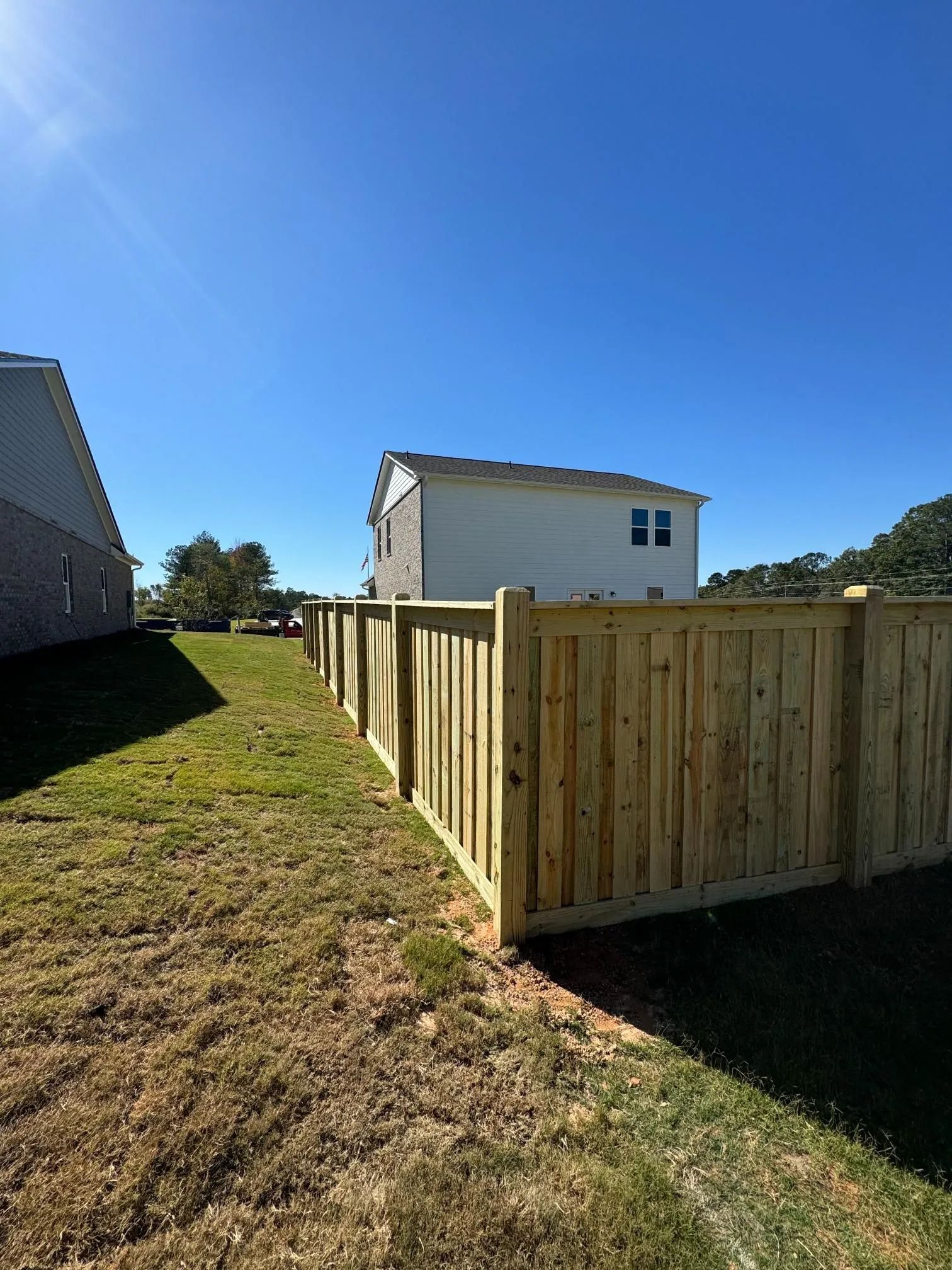 Wooden fenced yard on a grassy slope beside a house under a clear blue sky