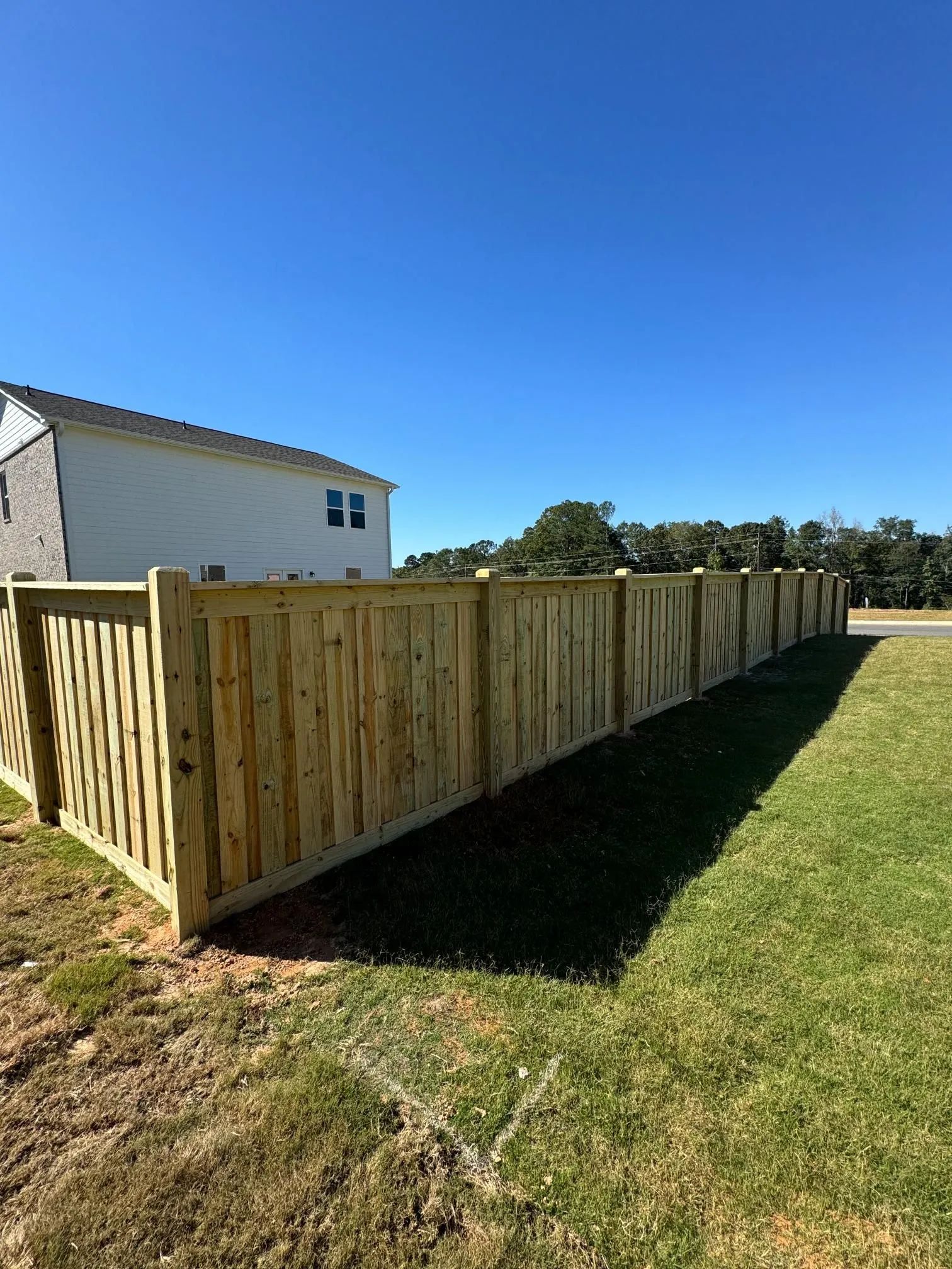 Wooden fence in a grassy yard under a blue sky, next to a white house.