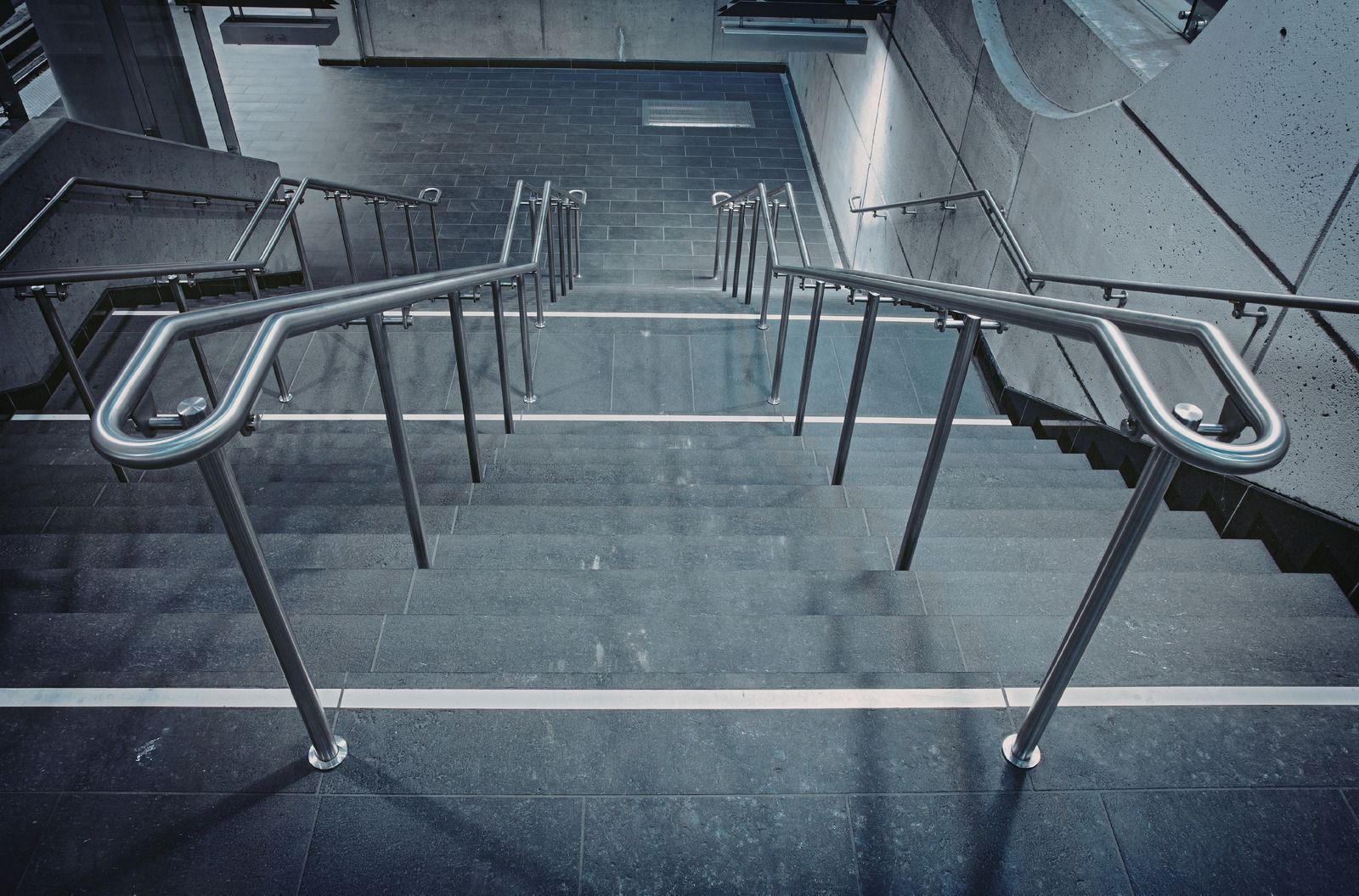 Brown deck railing with horizontal cables against a backdrop of trees, lawn, and road.