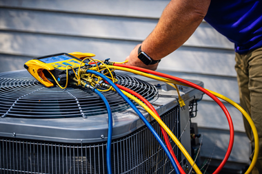 A technician uses a yellow manifold gauge set to service an outdoor air conditioning unit.