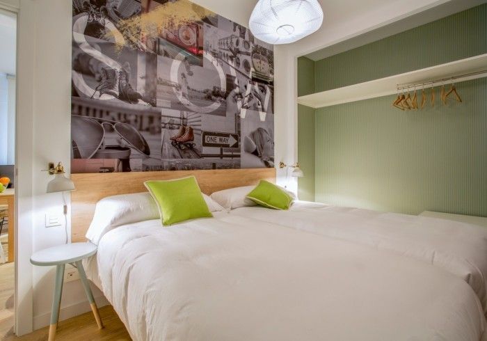 Habitación luminosa con cama blanca, almohadas verde lima y una pared decorada con un mural junto a un armario abierto.