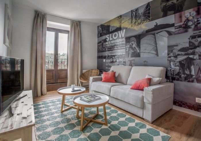 Sala de estar moderna con sofá beige, alfombra estampada en color turquesa y un gran mural de paisaje urbano en la pared.