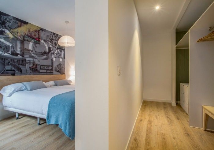 Dormitorio moderno con cama blanca, manta azul, cuadro en la pared y pasillo que conduce a un baño.