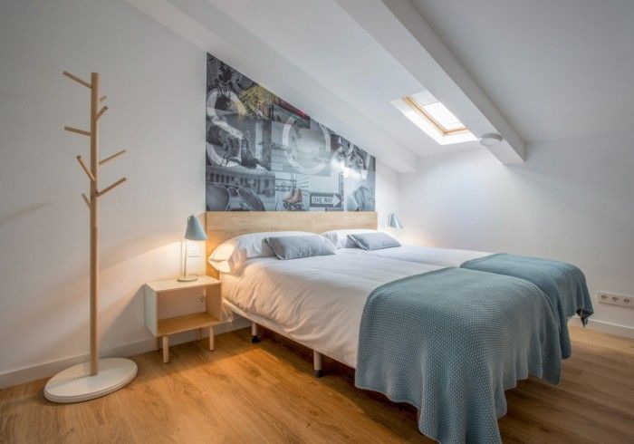 Luminoso dormitorio abuhardillado con cama, lámpara de mesilla de noche, claraboya y perchero de madera.