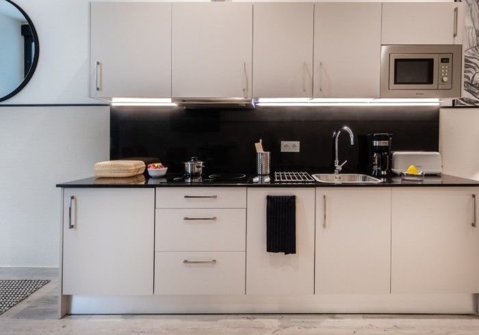 Cocina moderna con gabinetes blancos, salpicadero negro, fregadero, microondas y electrodomésticos de encimera.